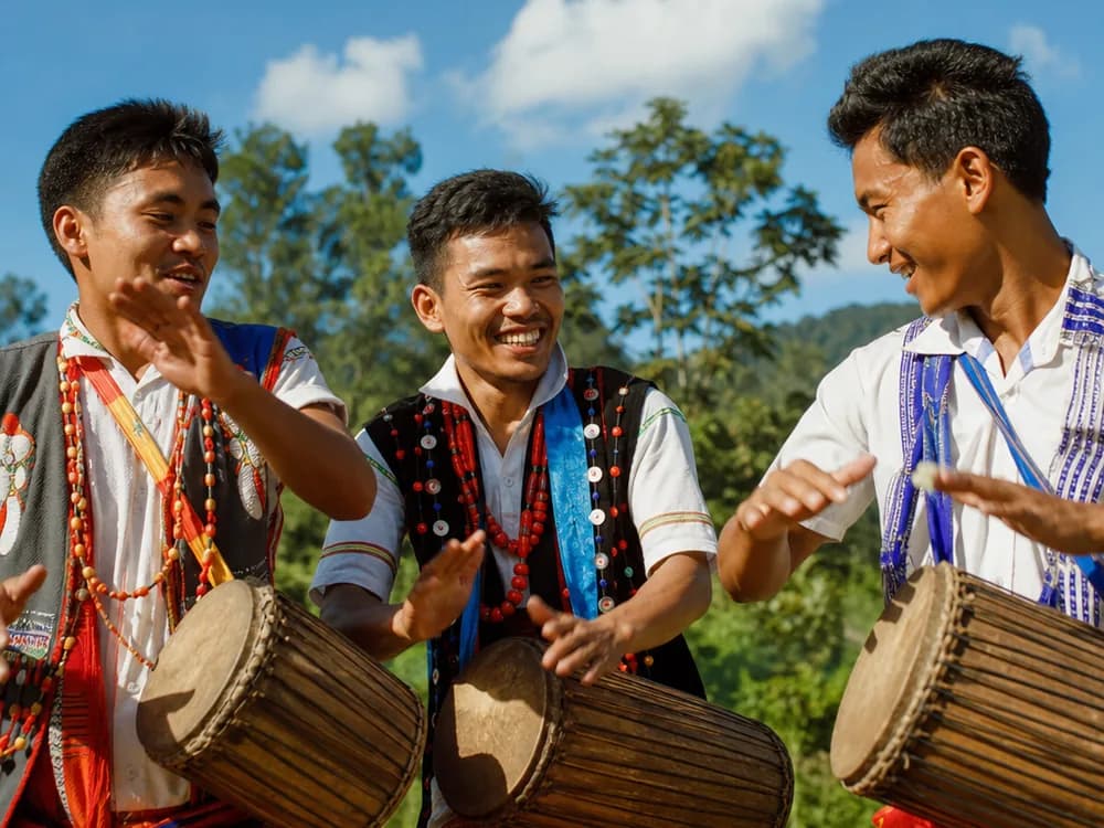 Drummers in traditional dress playing long hand drums outdoors in bright sunlight