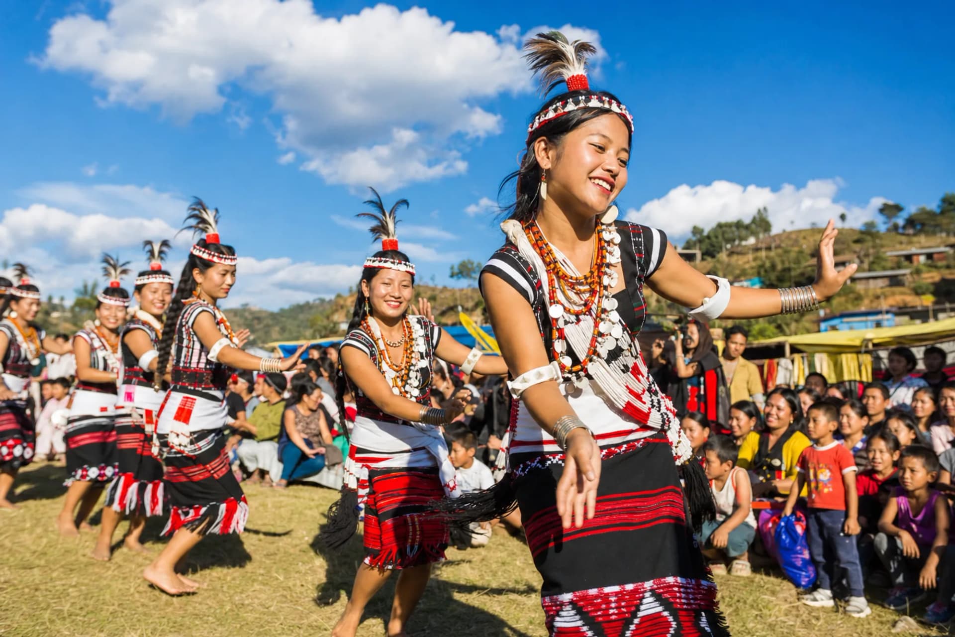 Dancers in bright traditional dress performing at an outdoor festival ground in Northeast India in daylight