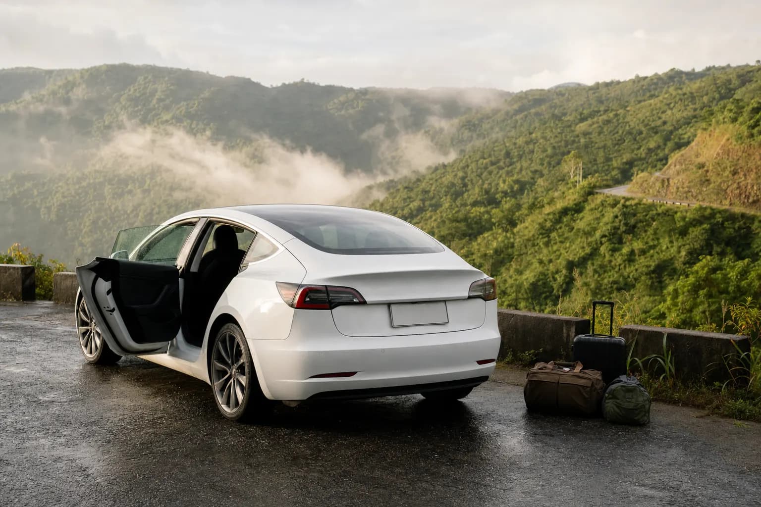 A white electric sedan waiting at a misty hill-road viewpoint with travel bags beside it